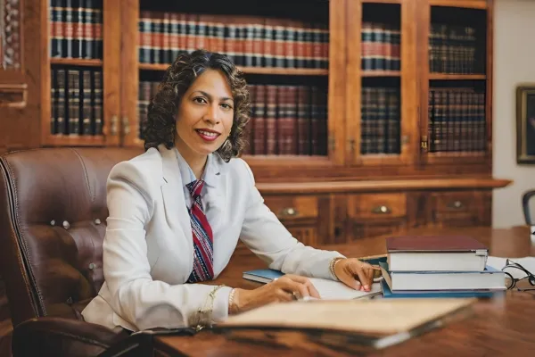 A woman in a suit, representing a local education law attorney in Bergen County, sits at a desk with a bookcase in view